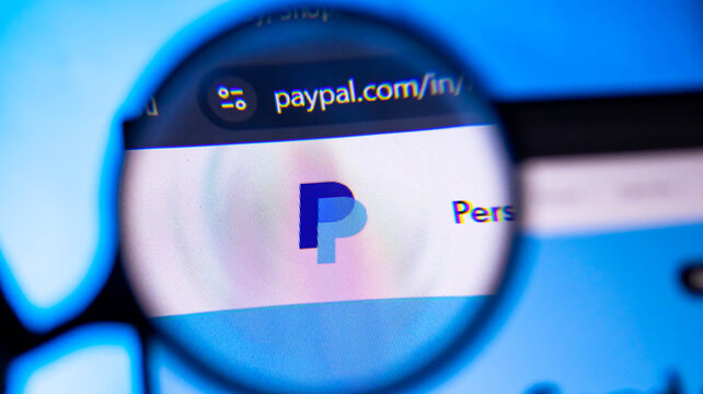 Magnifying glass focused on paypal logo and website url on digital screen.