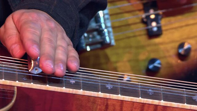 Detail closeup of male musician playing slide on lap steel guitar