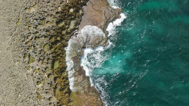 Aerial top-down view captures turquoise Caribbean waves crashing over volcanic rock coastline near Watamula Hole in Curacao