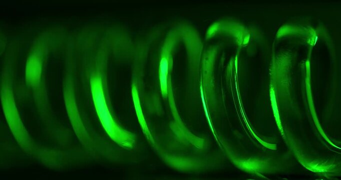 Nuclear atomic green illuminated spiral glass tube coil rotating on dark background.