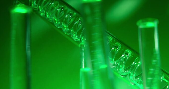 Slow motion glass test tubes and condenser with glowing green liquid in laboratory experiment.