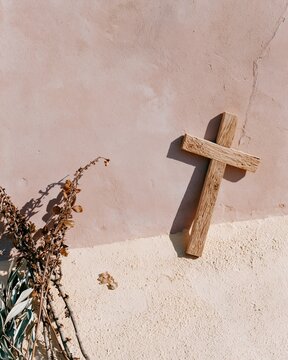 Pale pink and beige textured background with a small wooden cross and dried botanical branches for spiritual event invitations, funeral programs and religious cards