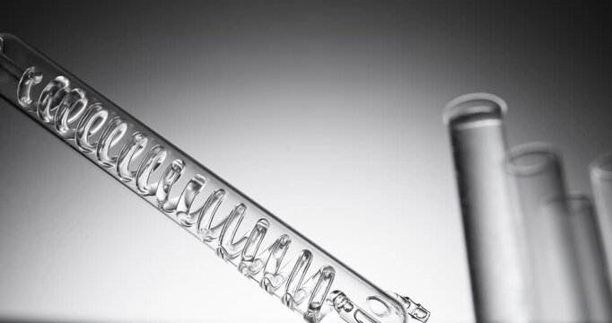 Slow motion glass coil pipette tilting above test tubes on laboratory bench setting.