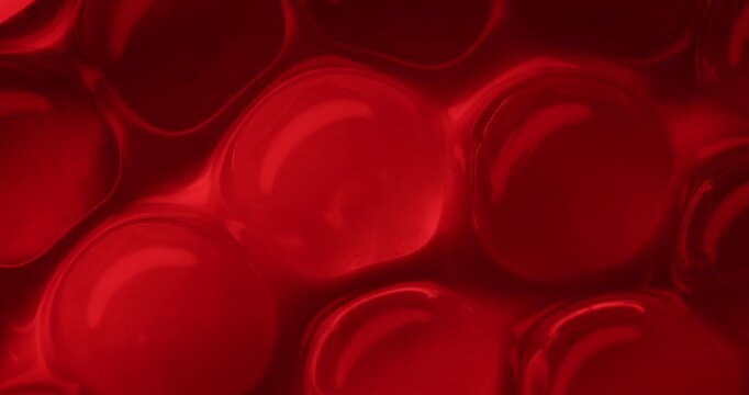 Slow motion macro close up of red gel spheres and bubbles shifting and undulating on glossy translucent surface, concept experimental with microscope for blood cell structure.