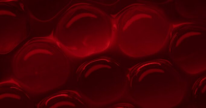 Slow motion panning close up of red translucent gel bubbles and spheres on glossy tabletop in studio, concept experimental with microscope for blood cell structure.