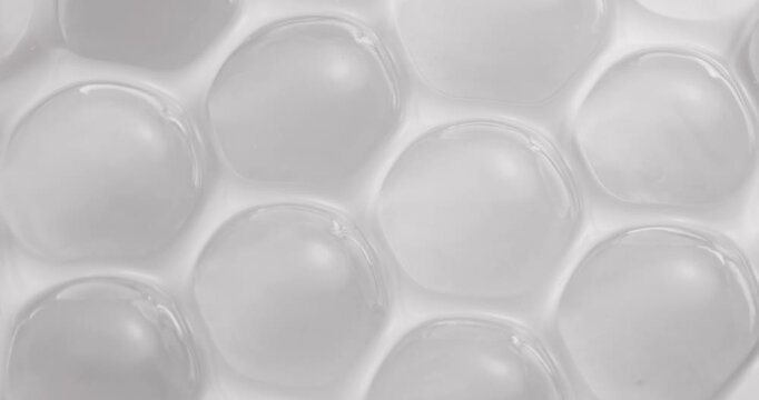 Slow motion close up of translucent gel bubbles shifting on white tabletop surface in studio.