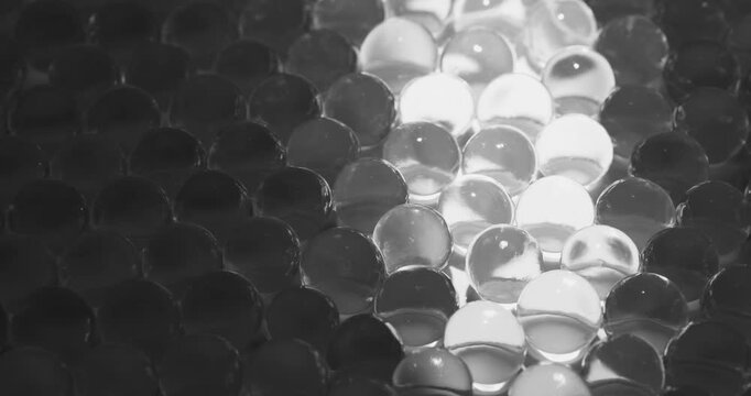 Slow motion glass marbles beads spheres on dark tabletop illuminated by moving light strip close up, concept experimental with microscope for cell structure.