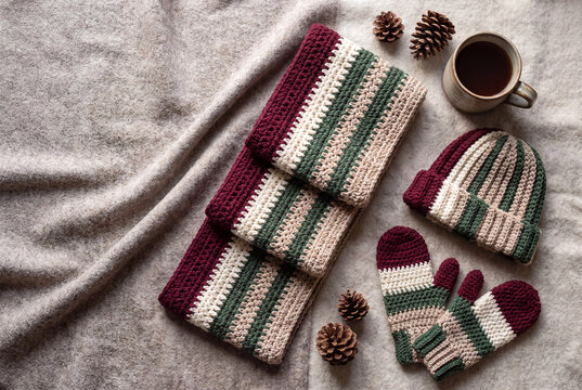 Crochet winter accessories photo with striped scarf hat mittens coffee and pinecones