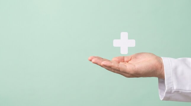 Doctor holding a white medical cross symbol on an open palm, representing healthcare, first aid, and medical insurance concept on a green background