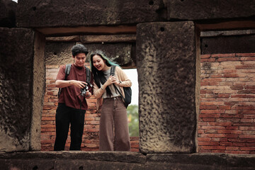 Obraz premium Young Asian travelers reviewing photos on camera at ancient temple ruins, cultural heritage tourism, travel adventure and exploration