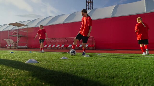 Womens soccer players practicing dribbling and control skills on synthetic turf during organized outdoor team training session under bright daylight conditions