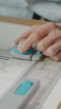 Closeup of architect hands drafting detailed technical building plans with markers, ruler, and drawing tools on large sheet of paper at creative workspace