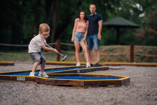 Little child learning mini golf with parents