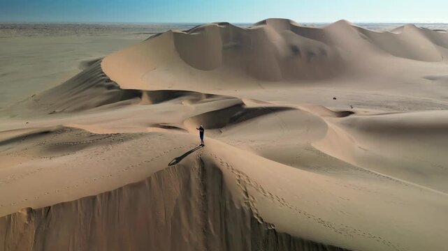 Aerial drone footage of vast desert sand dunes at sunrise. Cinematic wide shot of arid landscape with natural erosion patterns and golden light.