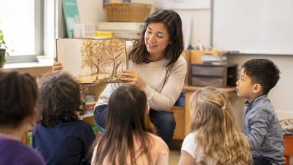 Fototapeta premium Smiling Female Teacher Reading an Illustrated Storybook to a Group of Attentive Preschool Children in a Bright Classroom Setting