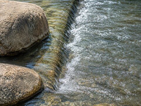 岩の間の段差を流れる澄んだ水が白い泡を立てる自然の景色。AIで生成
