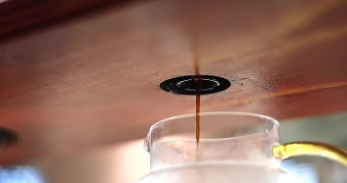 Fresh brewed coffee streams smoothly from the brewer into a glass server beneath wooden counter