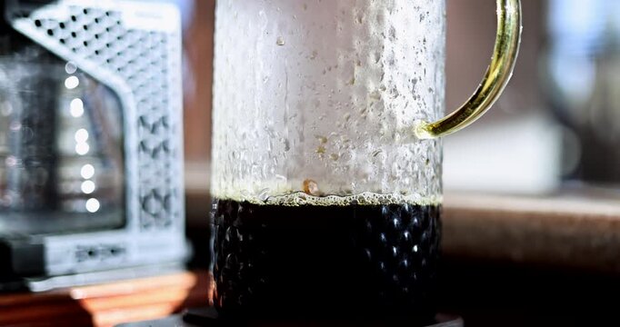 Fresh brewed coffee rests in a textured glass server on a digital scale beside brewing equipment, droplets bounce on surface