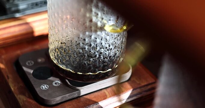 Glass coffee carafe sits on a digital scale while fresh brewed coffee finishes draining, medium static as it drips and shakes in slow motion