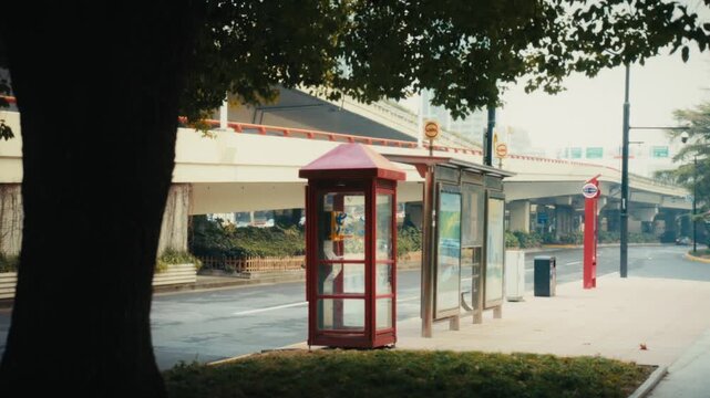 Street-level editorial shot of a vintage red telephone box and empty bus stop shelter on a quiet pavement near People's Square, Shanghai.