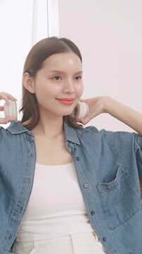 Happy Asian woman relaxing on sofa and listening to music with headphones, enjoying favorite song at home.