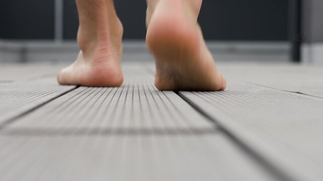 Rear view of barefoot man walking on composite terrace decking outside a modern home.