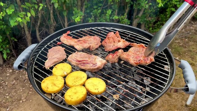 Meat and potatoes are grilled over a fire. The cook turns the pieces of meat on the grill. Backyard BBQ. High quality 4k footage