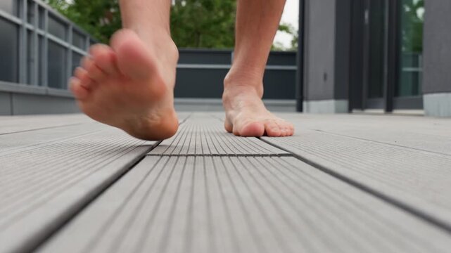 Close-up of bare feet walking on composite decking boards on an outdoor terrace.