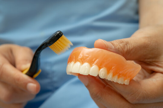 Asian senior woman patient clean teeth denture with toothbrush for chew food.