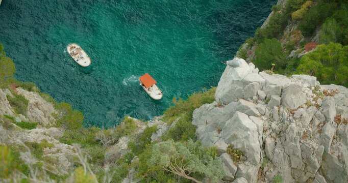 Boats cruising below rocky cliffs on turquoise sea coast near Capri Island, summer Italy