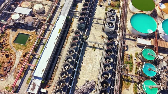 An industrial site with many cooling towers and storage tanks arranged in neat rows. The area is busy with machinery and equipment as work proceeds.