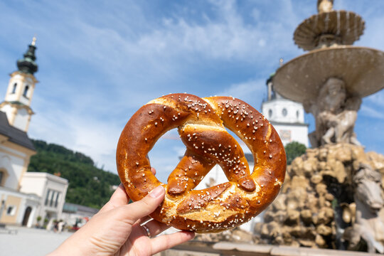 Pretzel with Salt in hand in front of a Fountain in Salzburg Residenzplatz, Austria bakery street food eating.