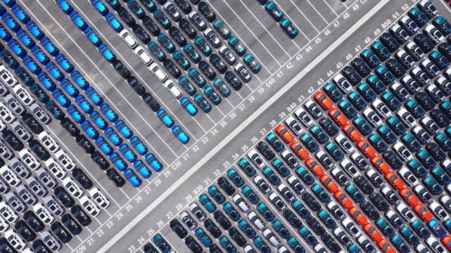 Aerial view of massive new car storage lot with neatly arranged multi-color sedans