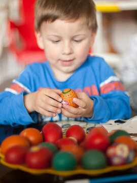 Child's gentle hands cradle a brightly painted Easter egg, surrounded by an array of colorful festive eggs on a golden tray indoors