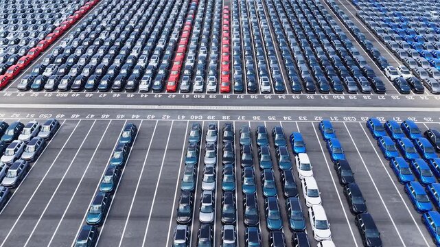 Aerial view of massive new car storage lot with neatly arranged multi-color sedans
