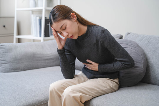 Close-up hands of young woman putting on her belly and feeling pain from cycle period on the sofa.