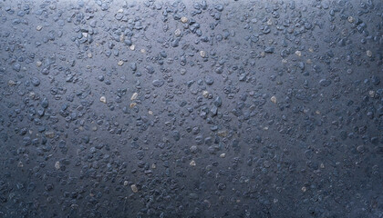 Fototapeta premium Close-up view of a dark, rough textured surface with embedded small stones, resembling asphalt or coarse concrete.