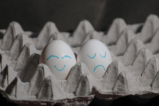 Chicken eggs with hand-painted funny faces in a cardboard tray. Trendy Easter background.