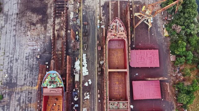 Workers are engaged in shipbuilding at a dock where several vessels are under construction. Tools and materials are scattered around the area.