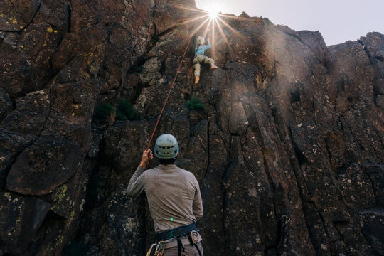 Man belaying woman climbing a sunny rock face