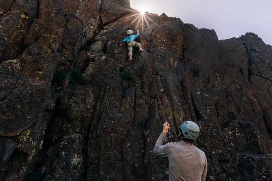 Young rock climber scales cliff with belayer support