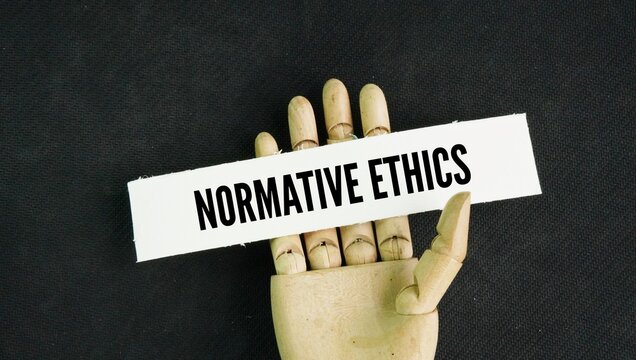 Hand and paper with the word Normative Ethics. the branch of moral philosophy that studies how people ought to act.