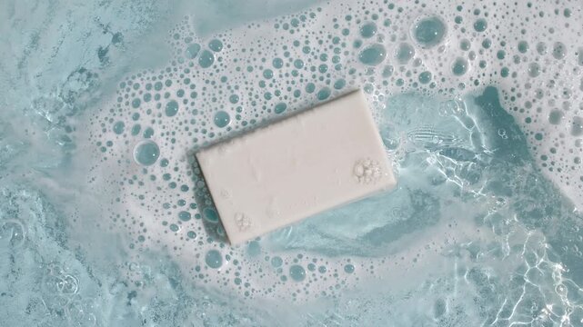 A bar of soap on a water surface with bubbles of white soapy foam. Concept of bath products, skin care products advertisement spa cosmetics. Body care and relaxation. High quality 4k footage