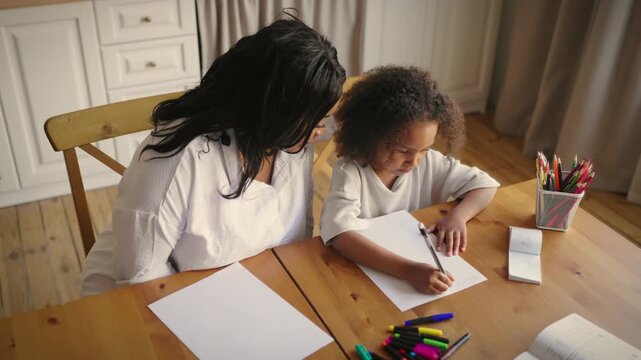 Black english teacher practicing spelling with little girl, home education. Cute studying and practicing to write letters in notebook, orthography of foreign language, school education