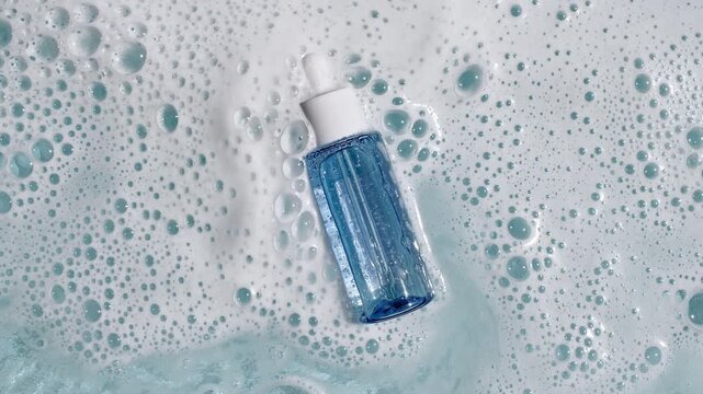 Bottle with a pipette for oil, toner, emulsion on water texture background surface with bubbles of white soapy foam. Women's cosmetics skincare, body care. Products advertisement spa, relaxation. 4k