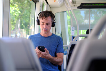 Adult man commuting on bus using smartphone and headphones © Cristina Garcia