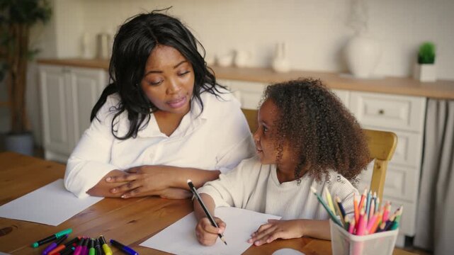 Teacher teaching smart little girl to write letters and words in notebook. Family time and parenting, african american mother and her preschooler daughter practicing spelling and english orthography