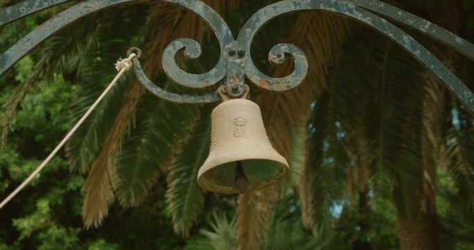 Old garden bell hanging among palm tree in warm Mediterranean summer light