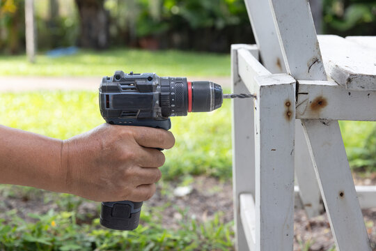 Man is drill a pilot hole on old chair wood before screw.