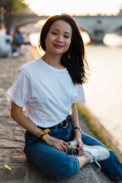 France, Paris, portrait of smiling young woman with camera at river Seine at sunset